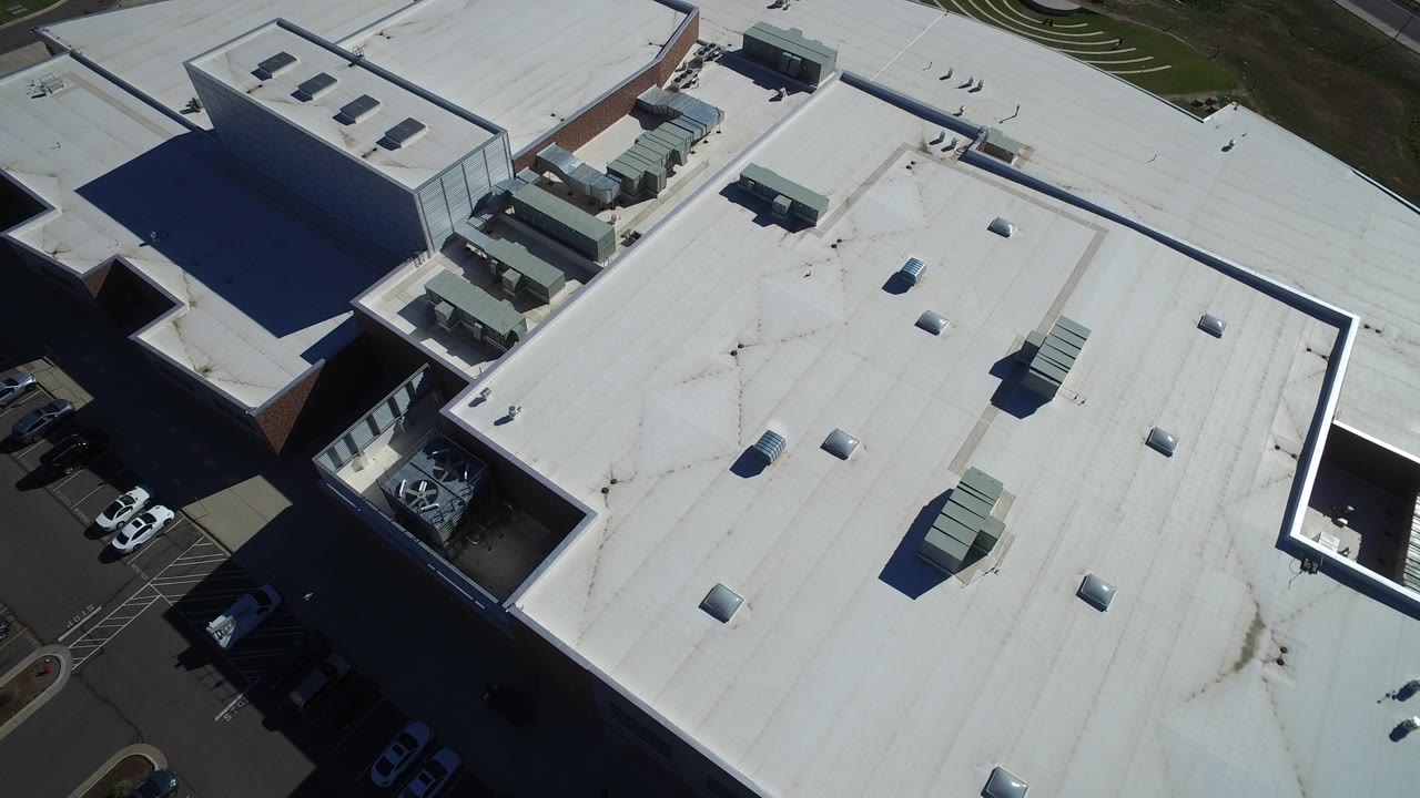 Overhead view of white shopping center rooftops and parking edges.