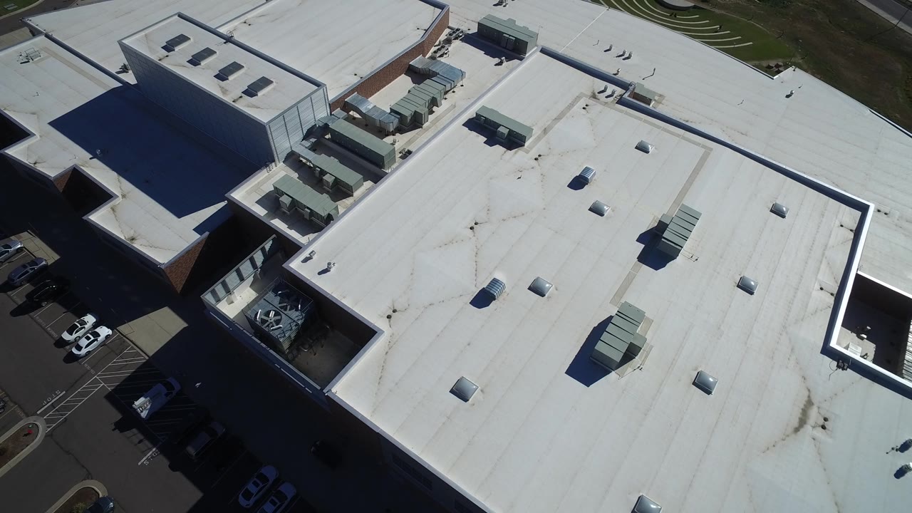 Second overhead frame in Hidden Lake, Colorado, showing the large white roof shifted slightly across frame, with HVAC boxes, skylights, adjacent parking, and no visible people.