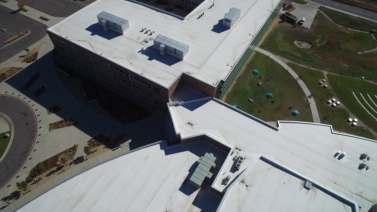 Opening aerial frame over a modern business complex in Hidden Lake, Colorado, showing white flat roofs, green lawn, curved walkways, road edges, and no visible people.