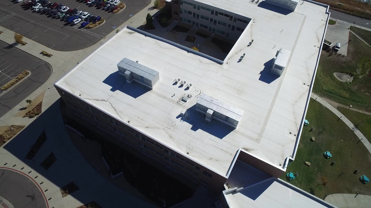 Aerial view of a white-roofed building beside a parking area.