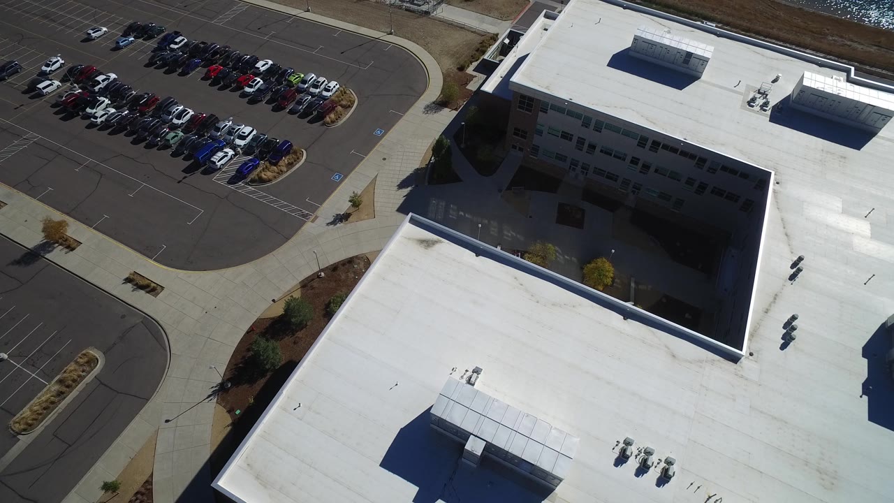 Drone view of roof edge, parking lot, and sidewalk network
