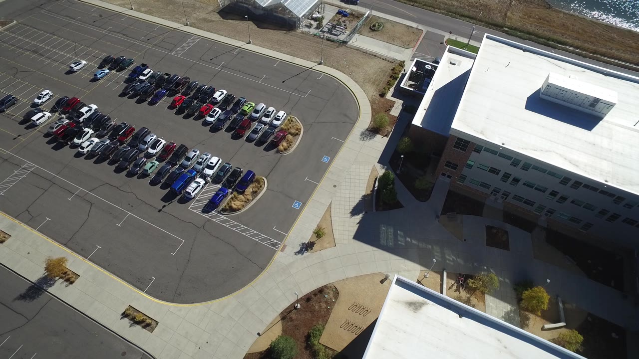 Second frame shows the Hidden Lake business lot from above, with the building roof filling the right side, clustered parked cars at center, empty stalls, and no visible people.