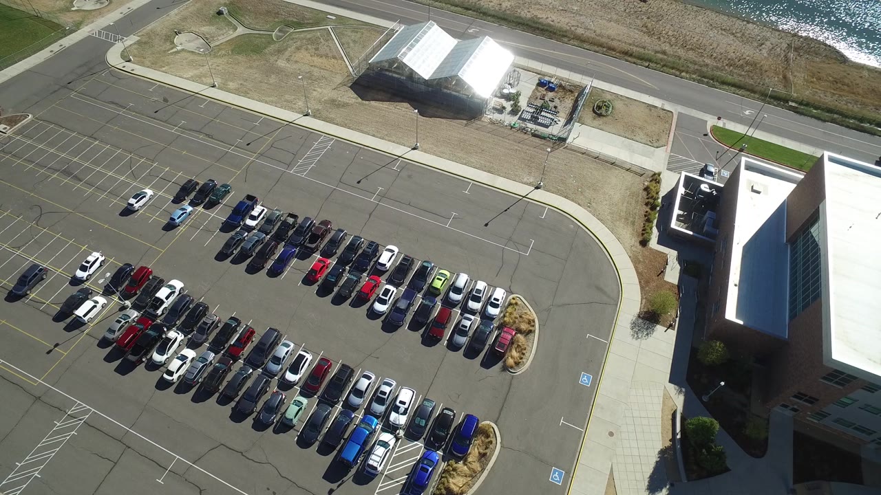 Hidden Lake, Colorado aerial frame with parked cars centered in marked rows, the modern building on the right, a road across the top, white-roofed structures beyond it, and no visible people.