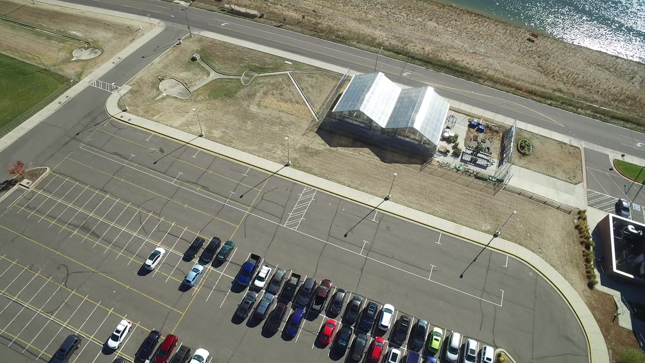 Overhead view of a parking lot, road, building, and lake edge.
