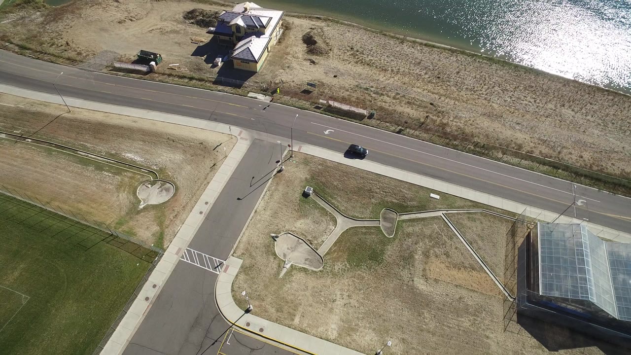 Aerial view of a road, lakeside house, dry grass, and dark car.