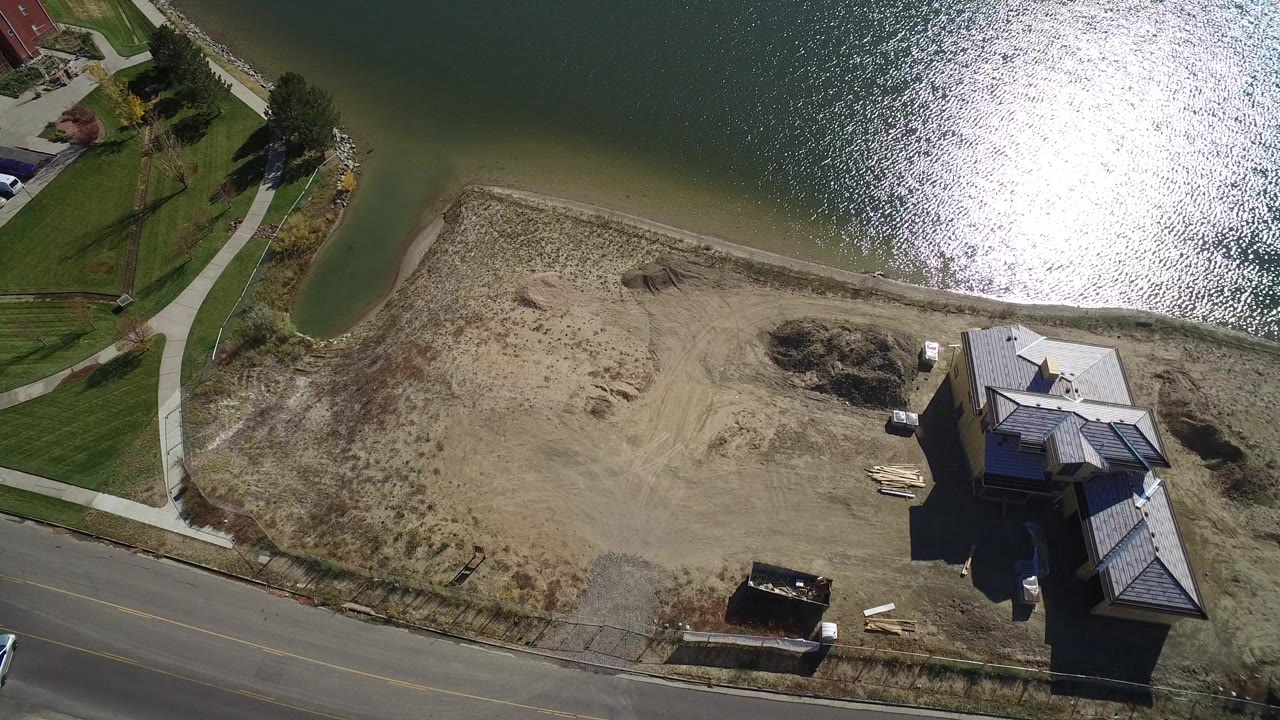 Aerial view of sandy lake beach, road, paths, lawns, and lakeside buildings.