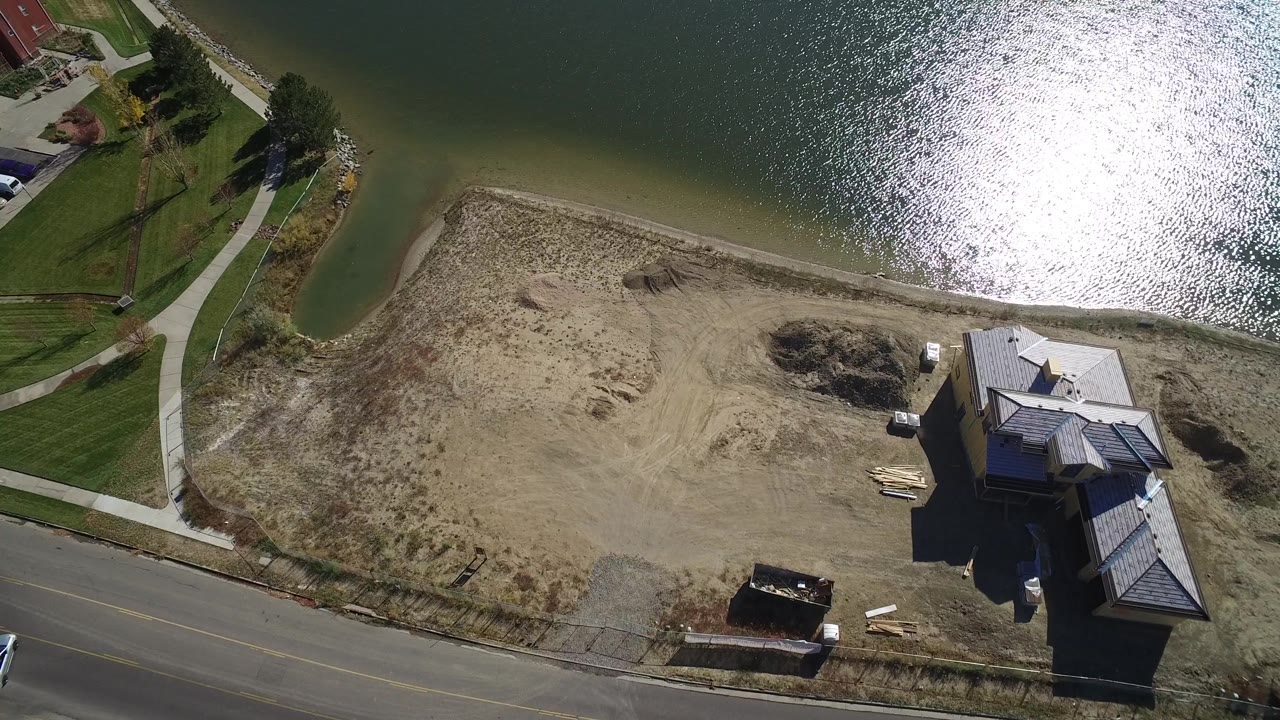Aerial view over Hidden Lake, Colorado, with the reflective water taking the upper frame and the sandy beach, road, sidewalks, lawns, and houses arranged below with no visible people.