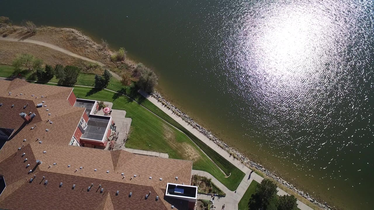 Overhead view of rooftops, lawn, path, shoreline, and sunlit lake water.