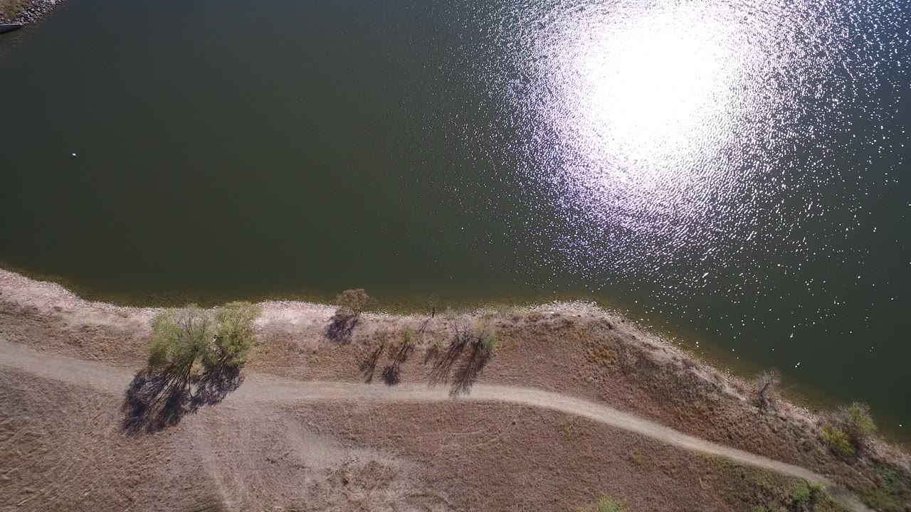 Drone view of rippled water, shore, dirt road, dry ground, and trees.