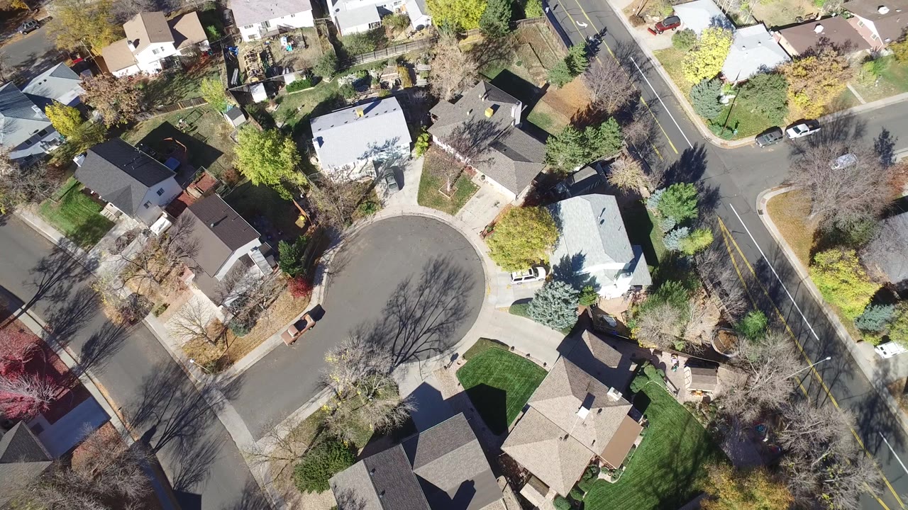 Top-down suburban block with houses, trees, and a larger road at right.