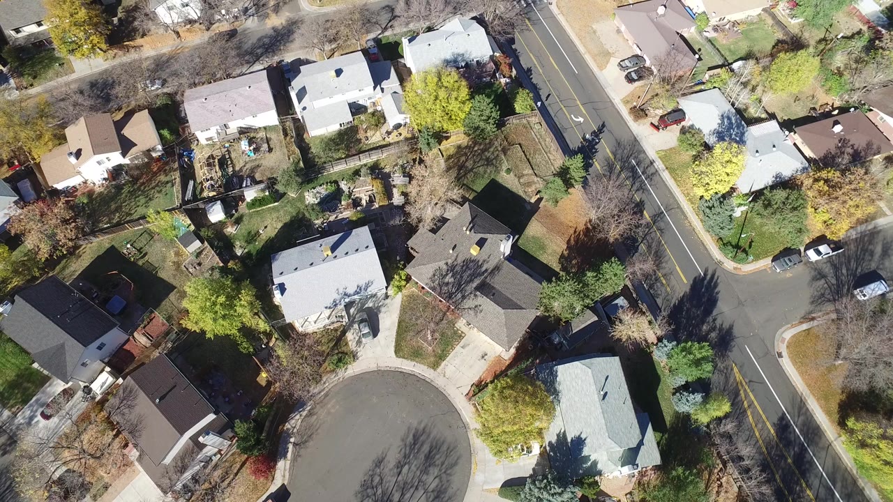 Overhead view of homes, trees, a cul-de-sac, and a two-lane road.