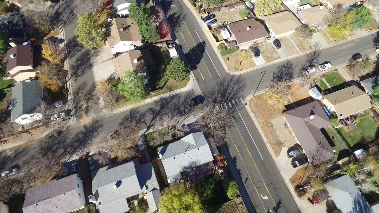 Overhead view of residential streets, homes, trees, and a dark car on the road.