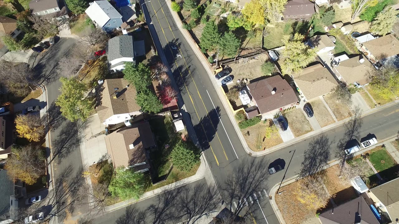 Overhead view in Hidden Lake, Colorado showing the road centered between homes, with pale lawns, parked cars, and leafless trees casting dark shadows.