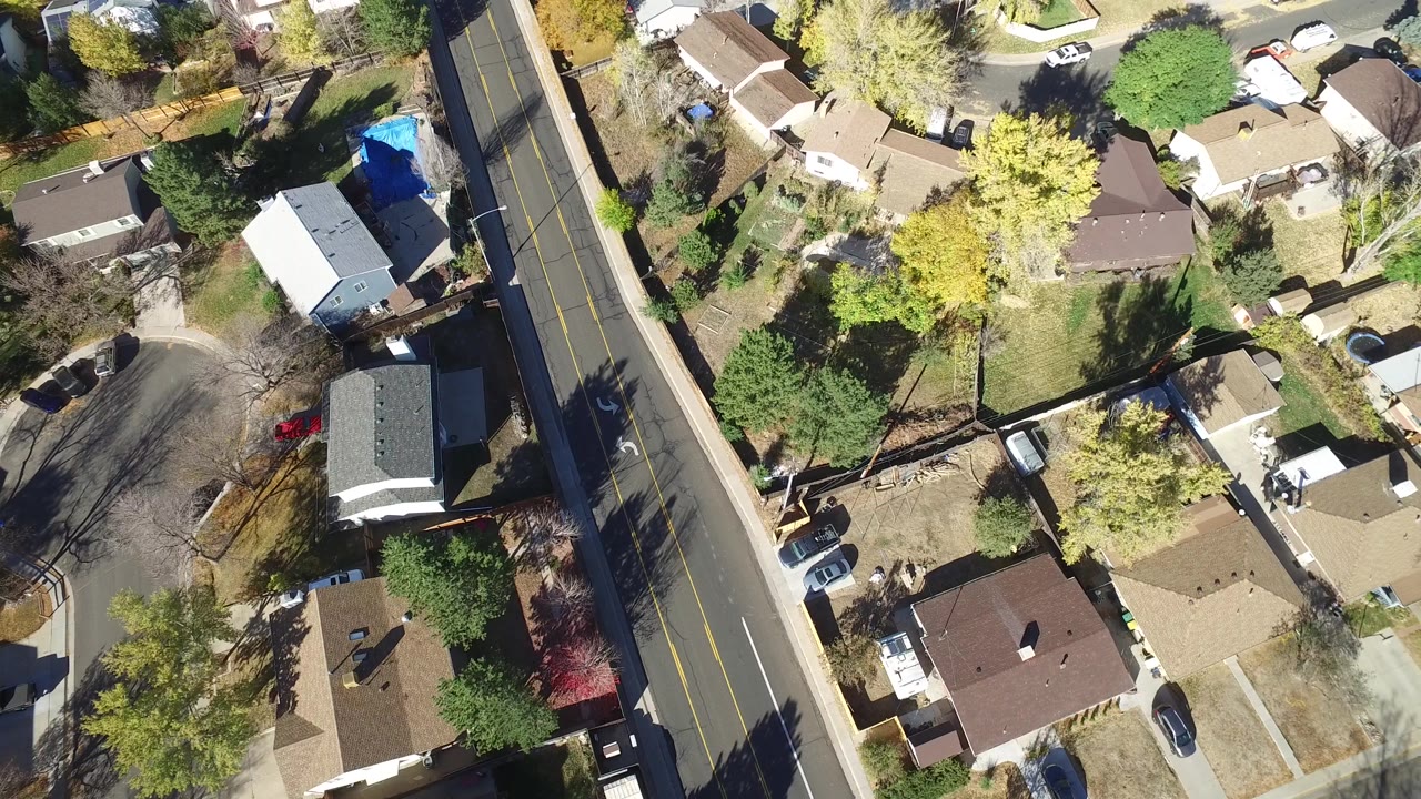 Second Hidden Lake, Colorado frame showing the same overhead neighborhood from slightly farther along the block, with rooftops, driveways, yellow trees, parked cars, and no visible people.