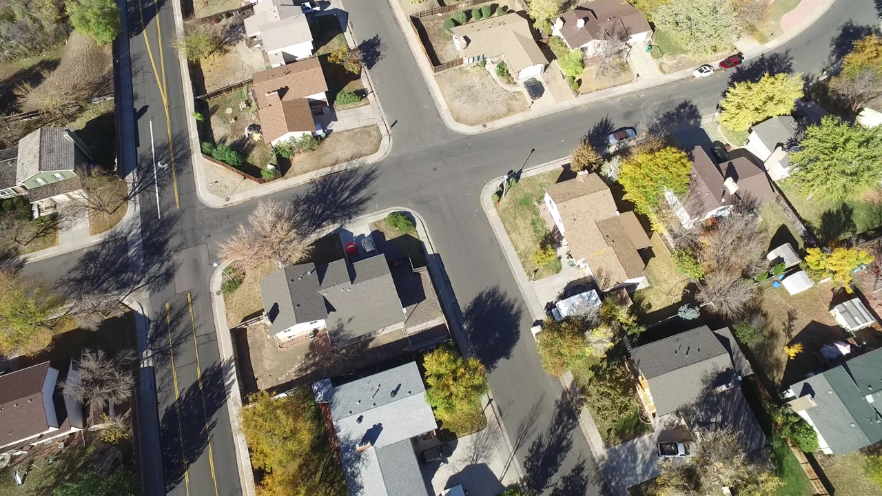 Overhead frame of Hidden Lake, Colorado showing a residential cross street, detached homes, tree shadows, driveways, and no visible people.