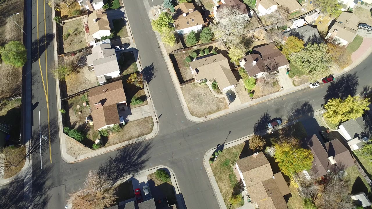 Overhead view of houses, streets, trees, and parked cars.