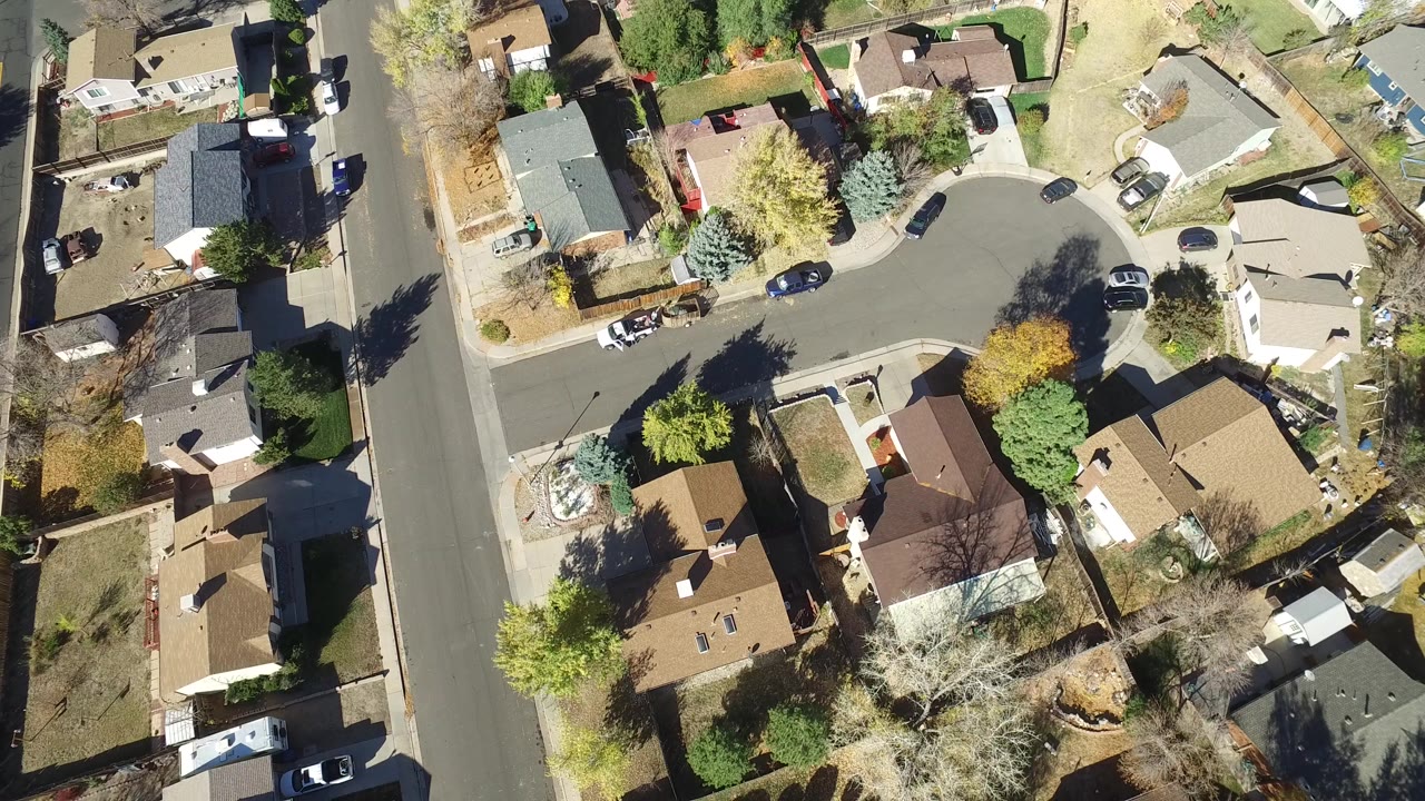 Overhead view of suburban houses, streets, yards, and parked cars.