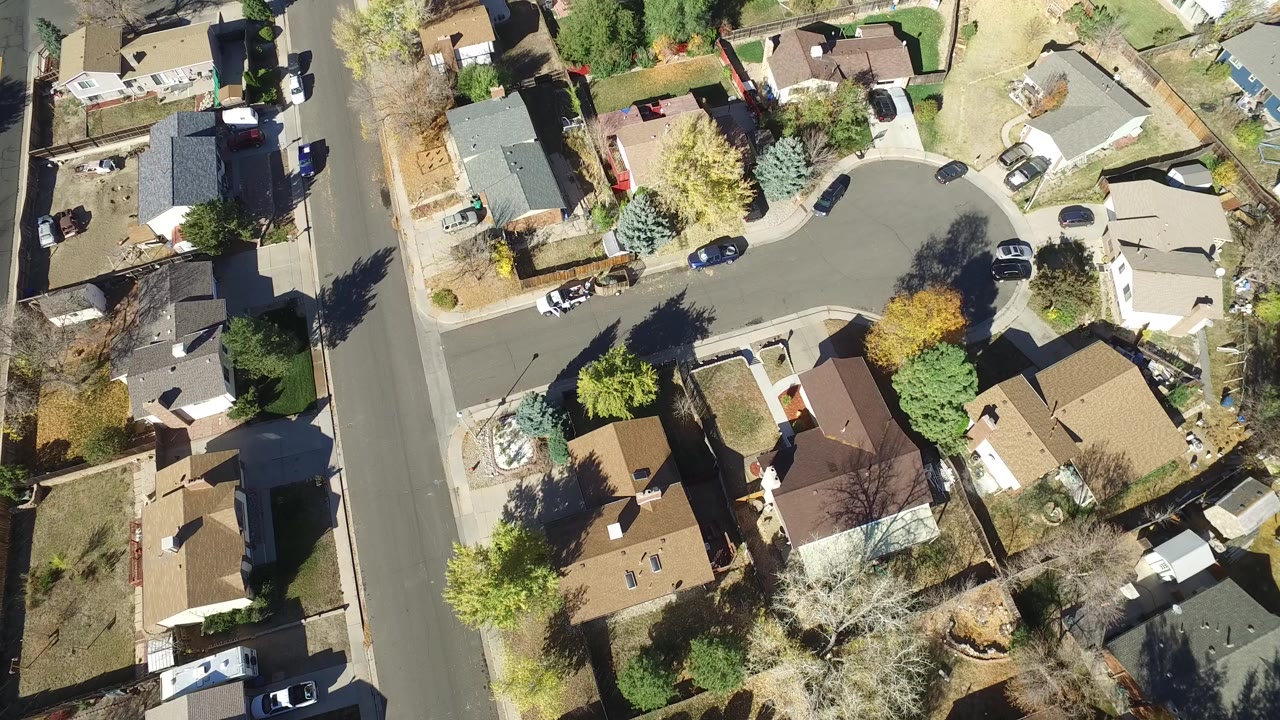 Aerial frame over Hidden Lake, Colorado with a cul-de-sac, surrounding homes, driveways, parked vehicles, fenced backyards, and yellow-green trees.