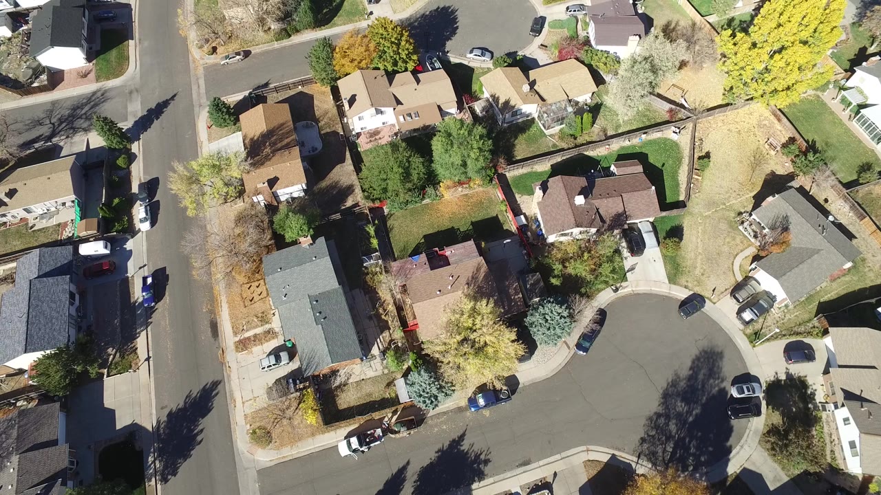 Aerial view of homes around a cul-de-sac with yellow trees and cars along the street.