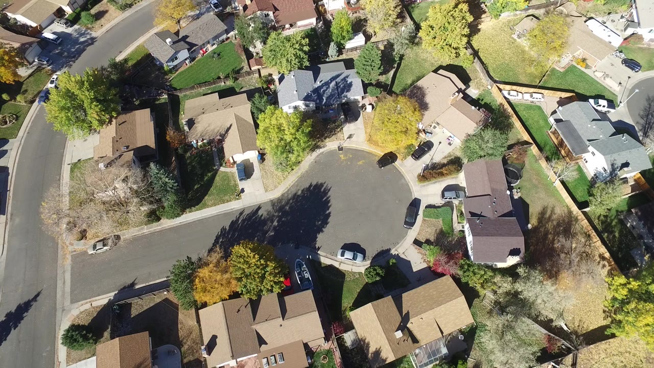 Overhead drone frame of Hidden Lake, Colorado homes around a curved street, with lawns, trees, parked cars, and no visible people.