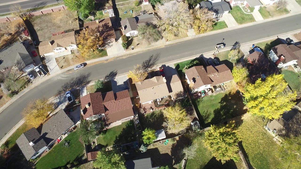 Aerial frame over Hidden Lake, Colorado showing several detached houses, fenced yards, green lawns, yellow trees, a nearby road, and no visible people.