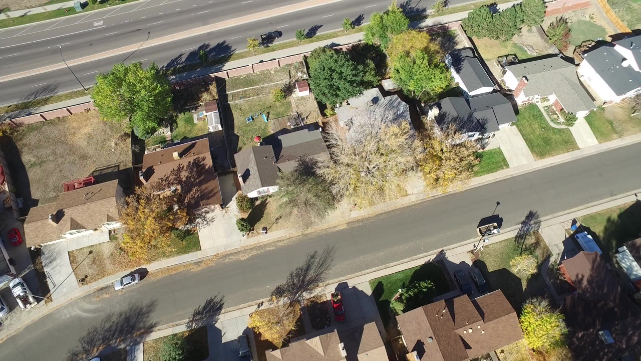 High overhead view of Hidden Lake, Colorado houses, lawns, parked cars, trees, a curving residential street, and a multi-lane road at the top, with no visible people.