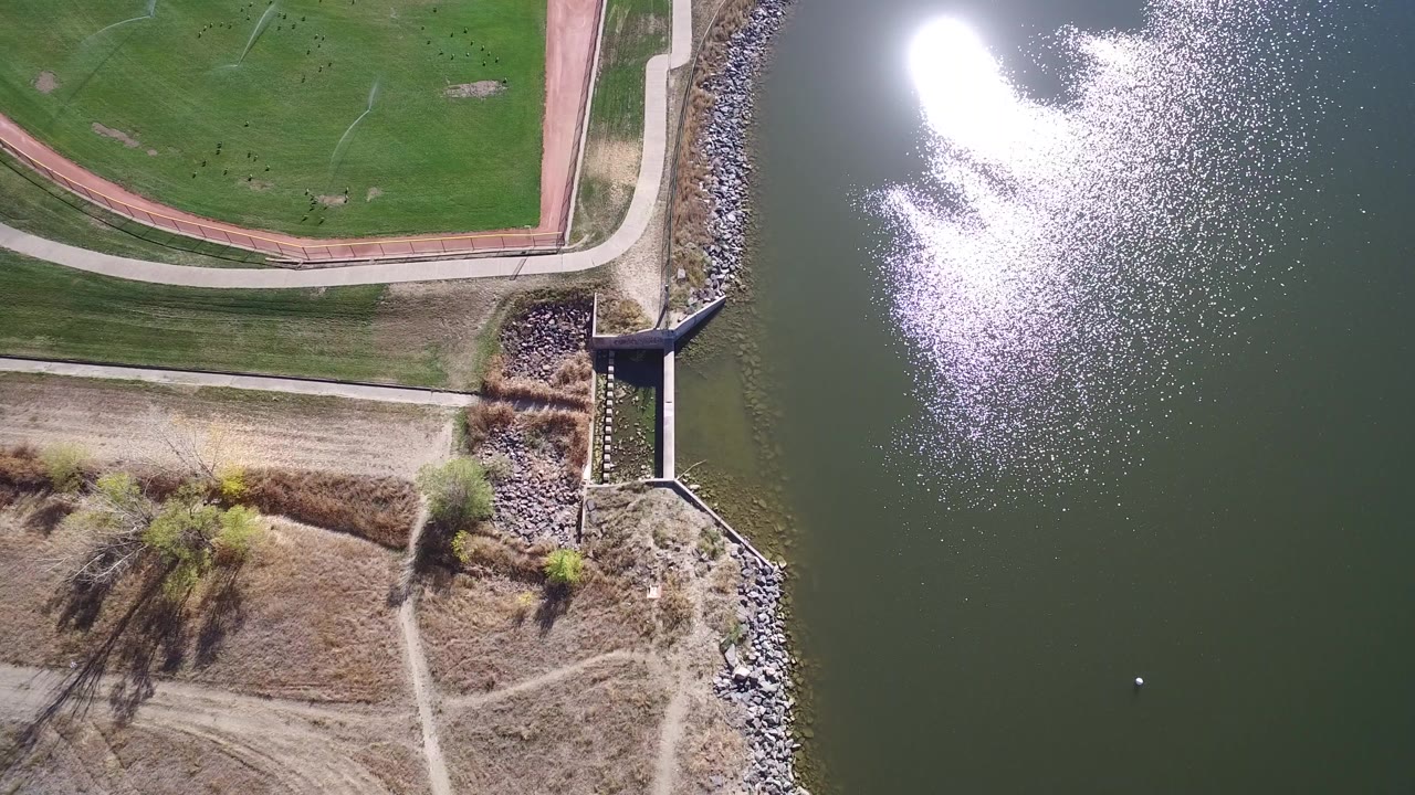 Aerial frame of a lake spillway, rock shoreline, grass, and paths.