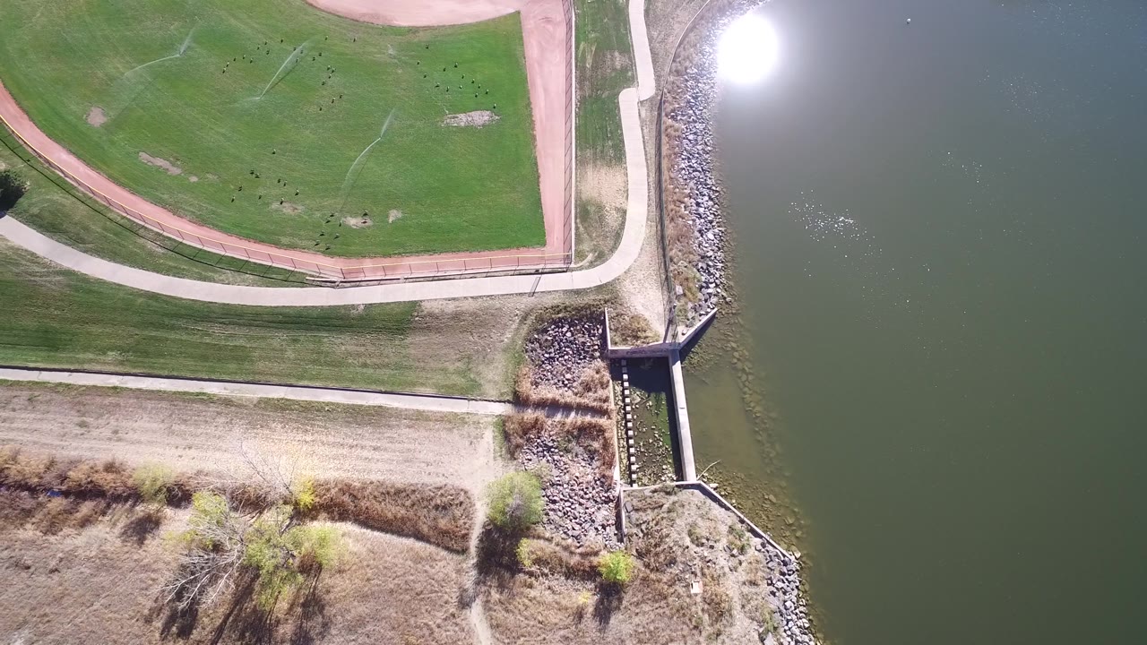 Overhead frame of green field, walking path, riprap, outlet structure, and lake water.