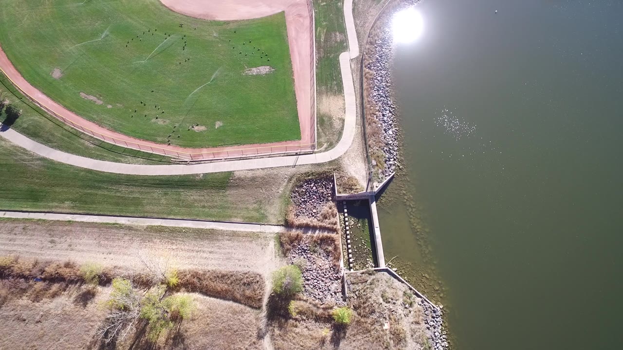 Top-down view of green course, tan path, riprap shoreline, and calm water.