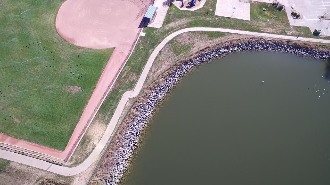 High overhead lakefront with grass, path, rocks, and paved park areas.