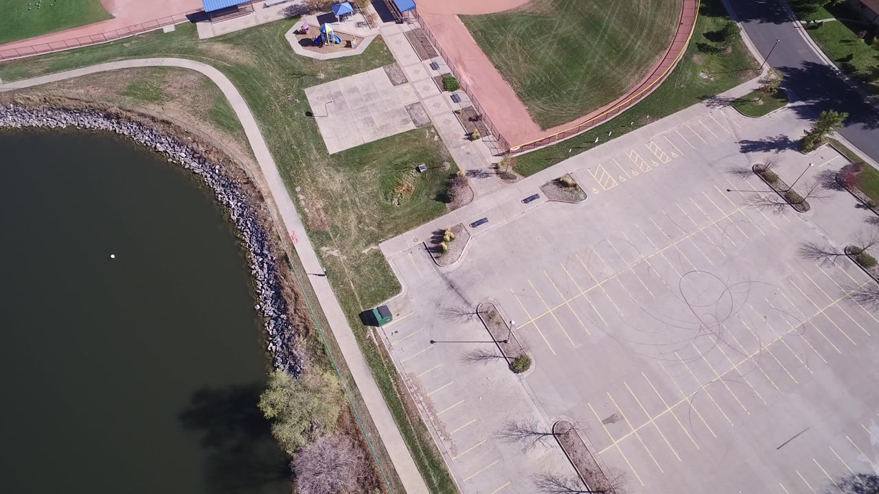 Second overhead frame in Hidden Lake, Colorado with the curved lake shoreline at left, pale parking stalls across the center, athletic grass at top, and no visible people.