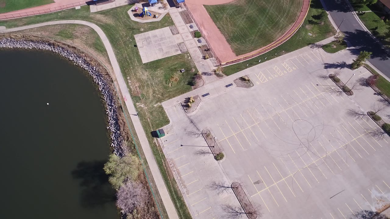 Top-down frame of a lakeside parking lot with baseball field edge and tree shadows.