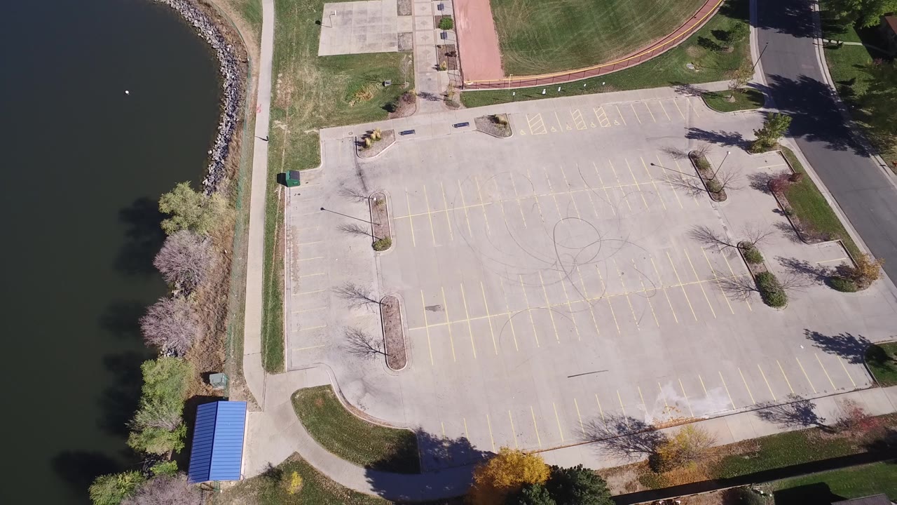 Top-down parking lot with road, grass, and lake shoreline nearby.