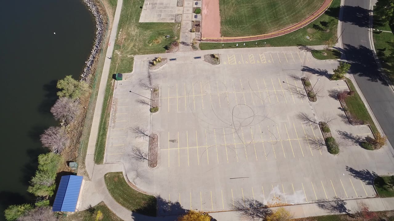 Overhead view of an empty parking lot beside dark lake water and park grass.