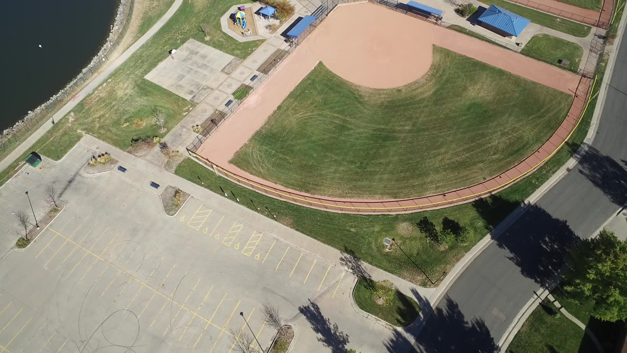 Aerial view of a lakeside recreation area with a ballfield, courts, road, and parking markings.