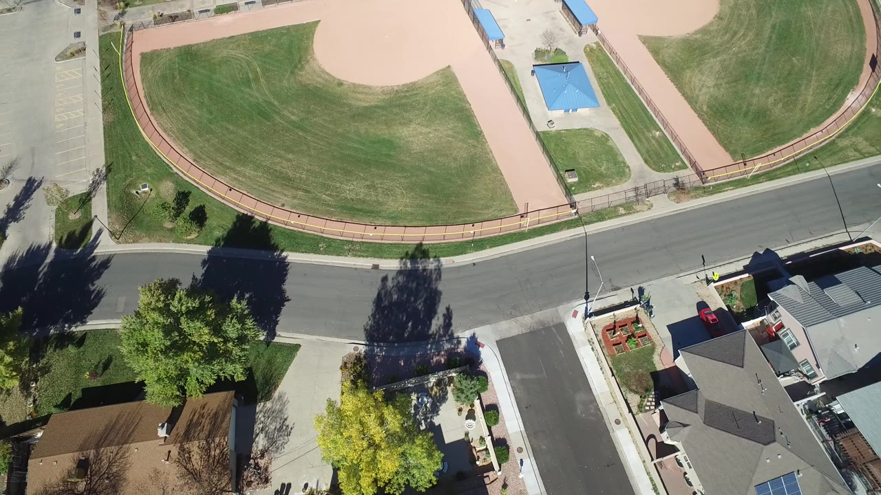 Overhead park lawn, curved path, street, trees, and residential roofs.
