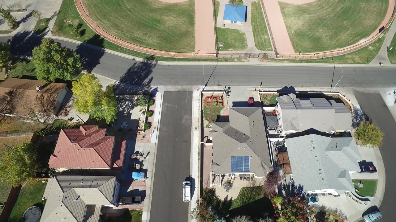 Aerial view of a curved residential street, roofs, trees, and a sports field.