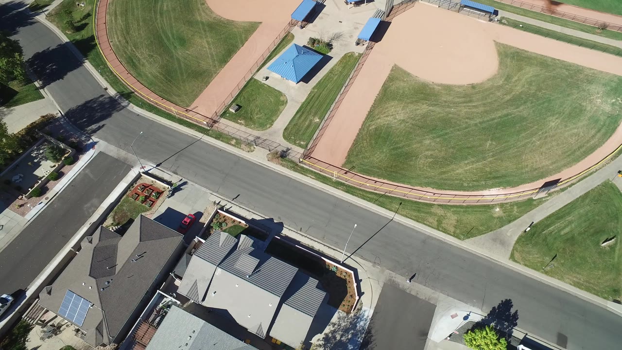 Overhead view of a suburban baseball diamond, road, and homes.
