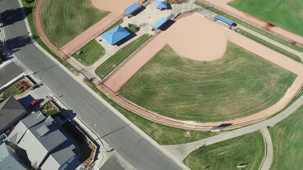 Overhead view of an empty baseball field beside a road and homes.