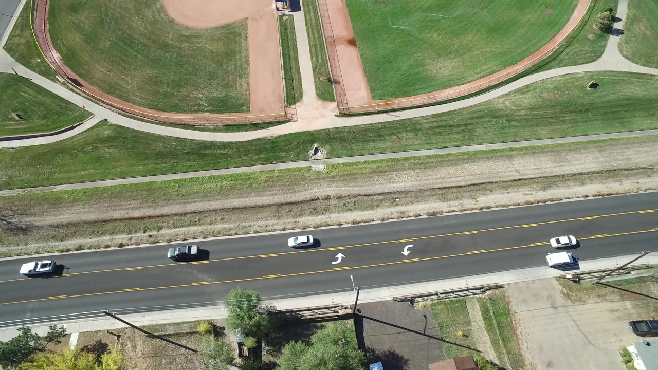 Aerial frame in Hidden Lake, Colorado, with cars spaced along the road, baseball diamonds at the top, green lawns, sidewalks, and no visible people.