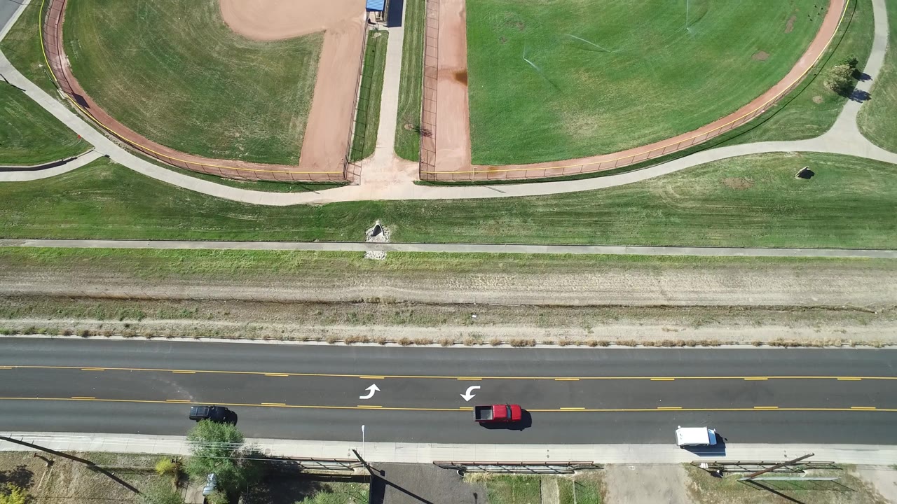 Top-down view of grass fields, paths, and cars on a road.