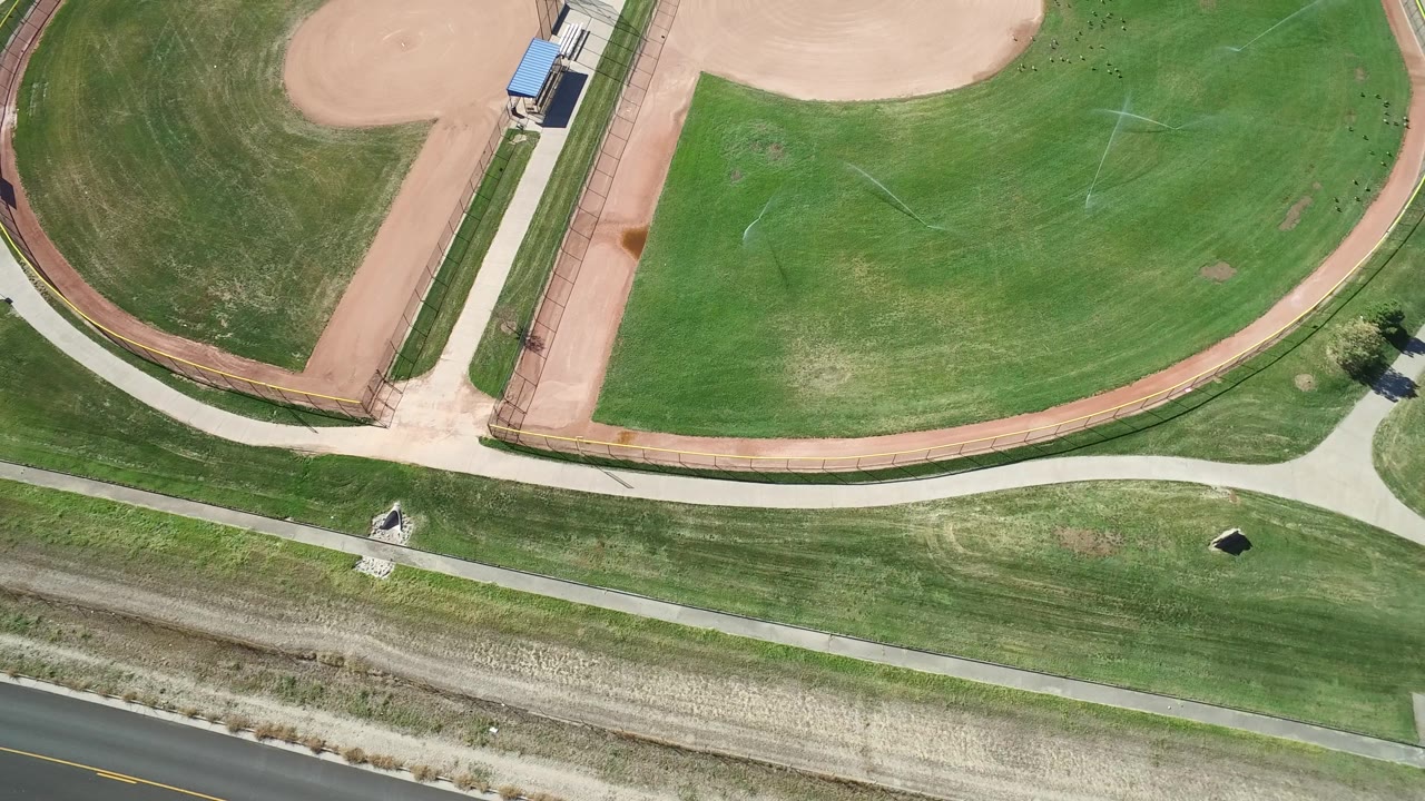 Top-down park view with baseball diamonds, grass, paths, and road.