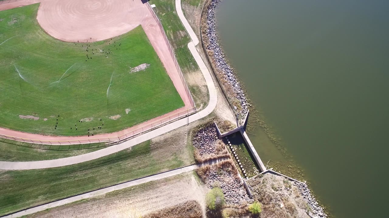 Top-down lake edge with sports field and shoreline structure.