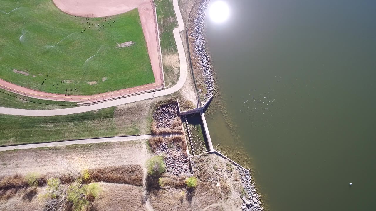 Top-down view of lake water, riprap, paths, and a small outlet structure.