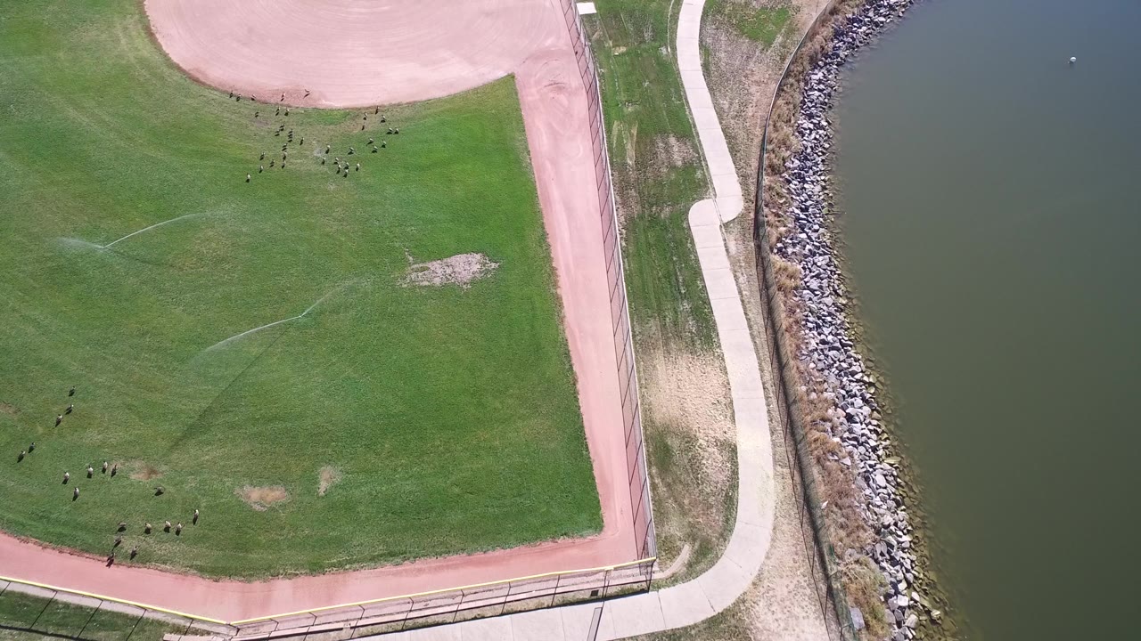Top-down grass field with path, walkway, rocks, and water.