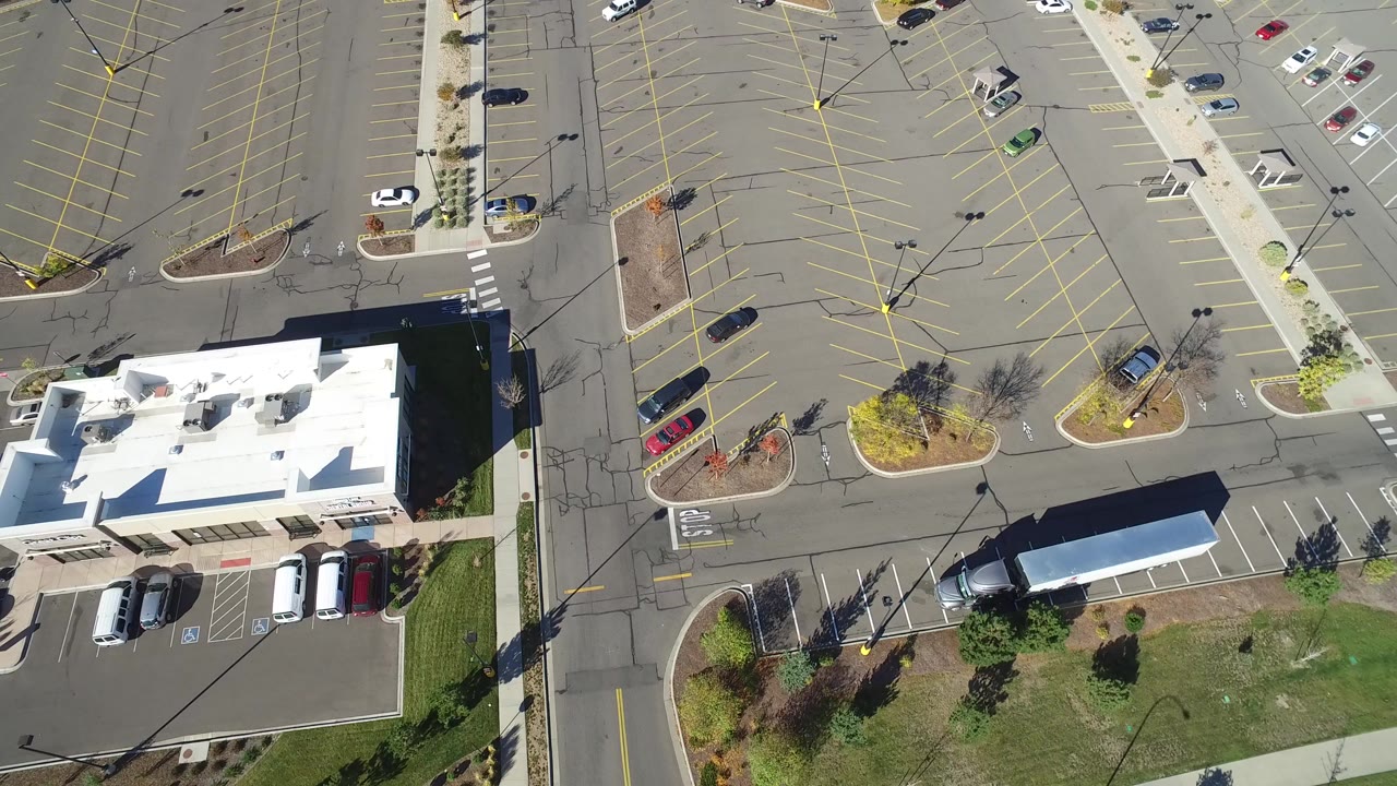Overhead view in Hidden Lake, Colorado showing a white-roofed commercial building, parked cars, marked asphalt spaces, sidewalks, and no visible people.