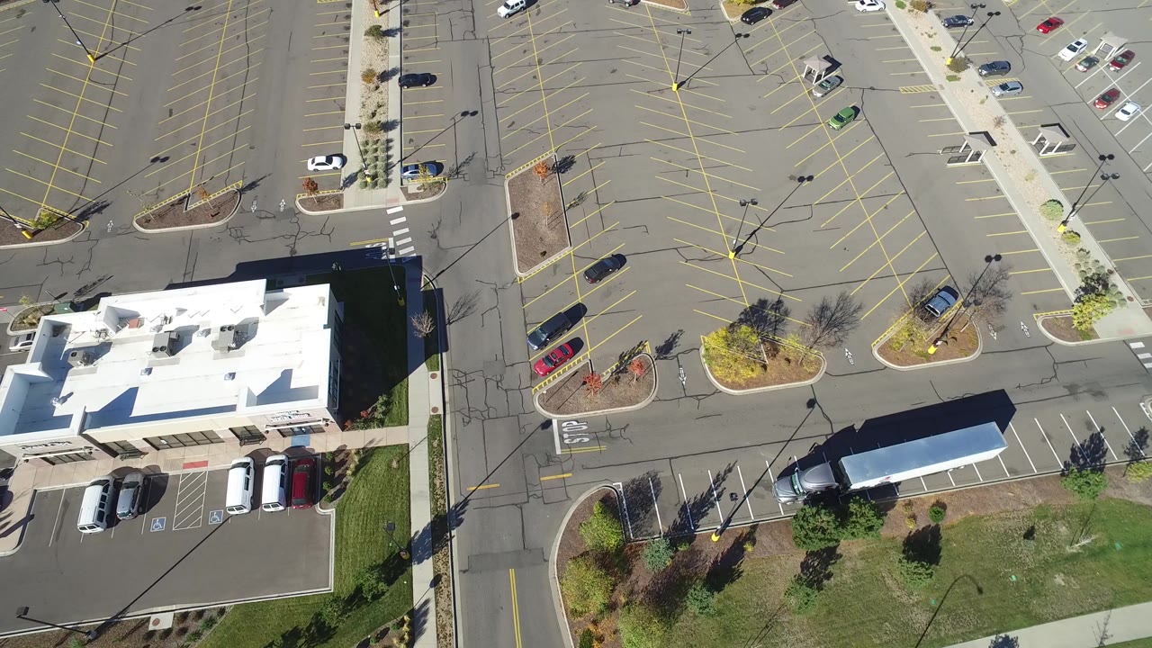 Aerial frame in Hidden Lake, Colorado with the white roof lower in view, empty yellow-lined parking rows above it, scattered parked cars, and no visible people.