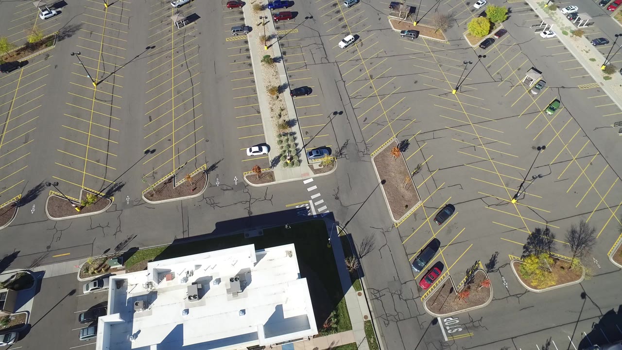 Overhead view of a mostly empty parking lot with yellow lines and a white-roofed building edge.