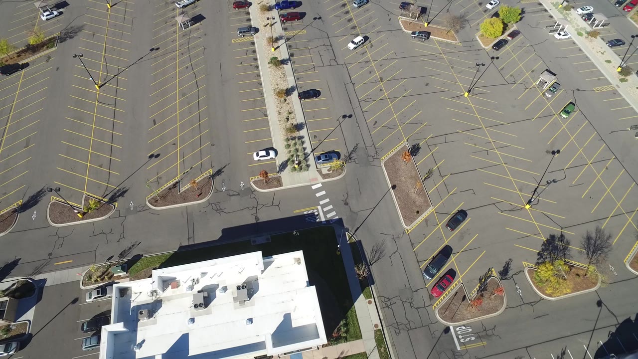 Overhead frame in Hidden Lake, Colorado showing the white-roofed building lower in frame, empty parking rows, several parked cars, and no visible people.