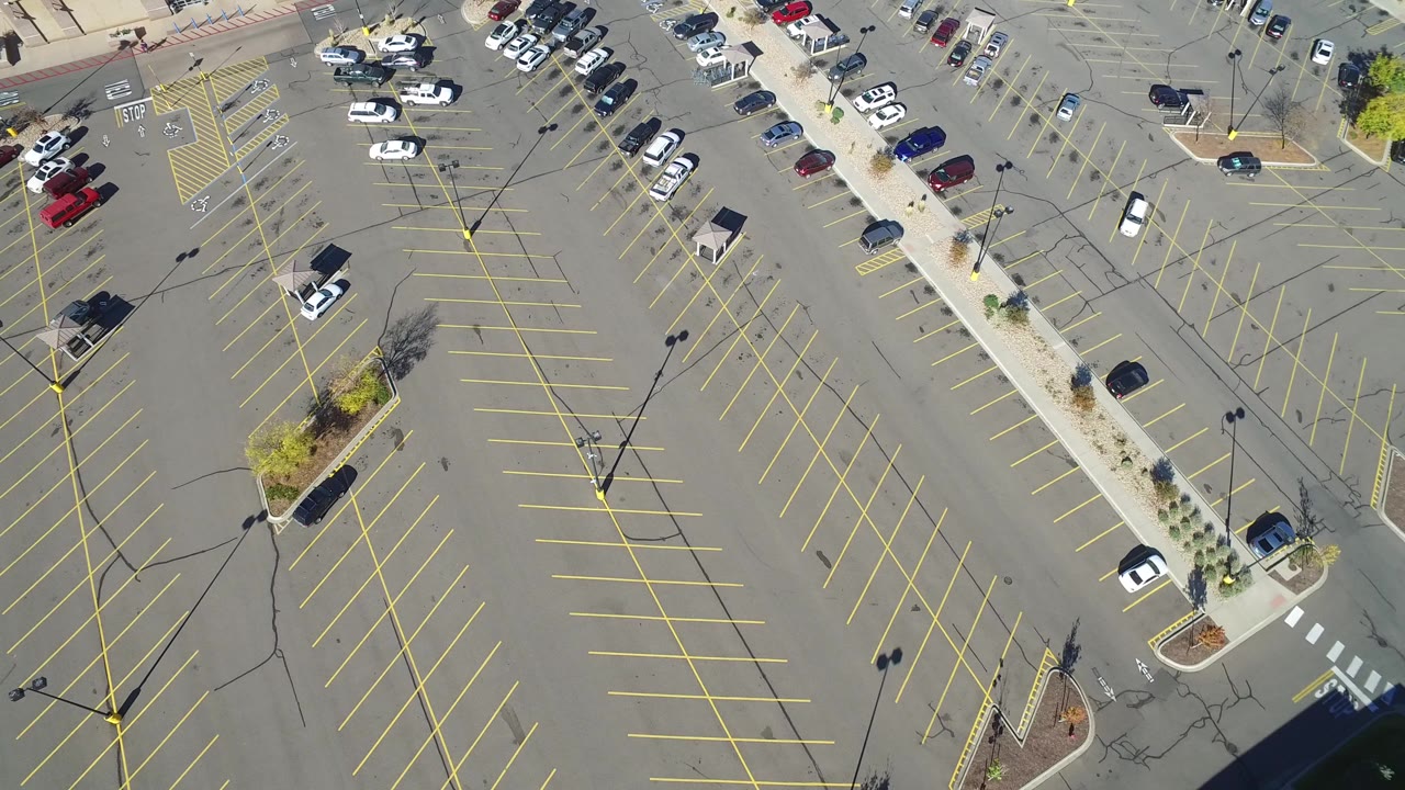 Aerial view of a large parking lot with yellow lines and scattered cars.